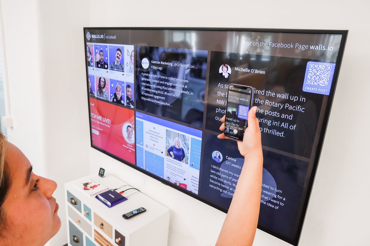 A woman uses a smartphone to scan a QR code on a digital wall display indoors.